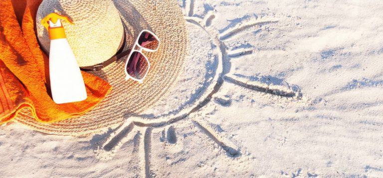 sunscreen and beach hat in sand