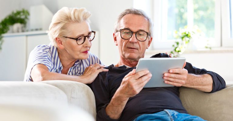 A man and a woman sitting on a couch and reading from a tablet