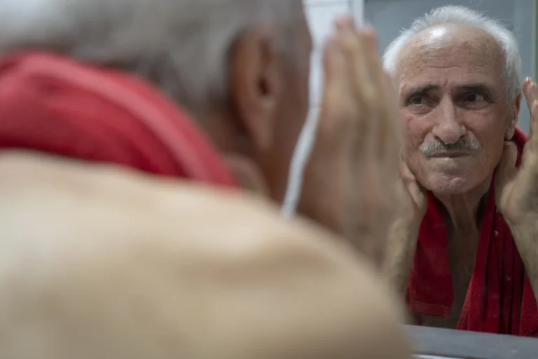 Older man examining a spot on his face in the mirror, concerned about a sore that is not healing