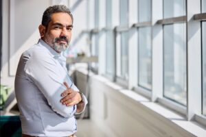 Man standing by large office windows in bright sunlight, representing everyday UV exposure through glass