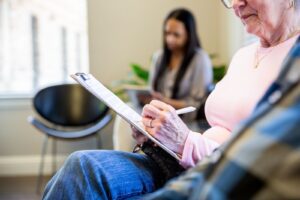 Older adult filling out paperwork on a clipboard in a medical waiting room before a dermatology appointment