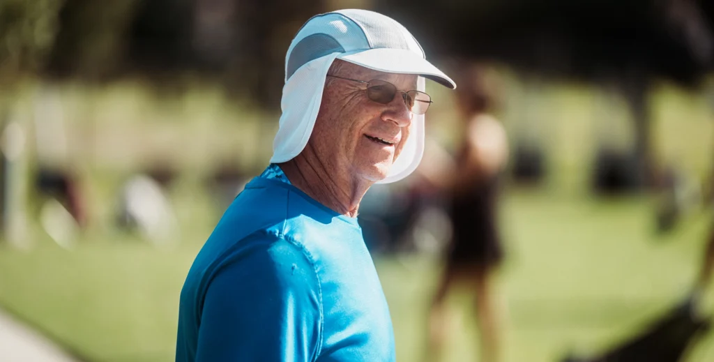 Older man wearing a sun-protective hat and shirt while outdoors in bright sunlight.