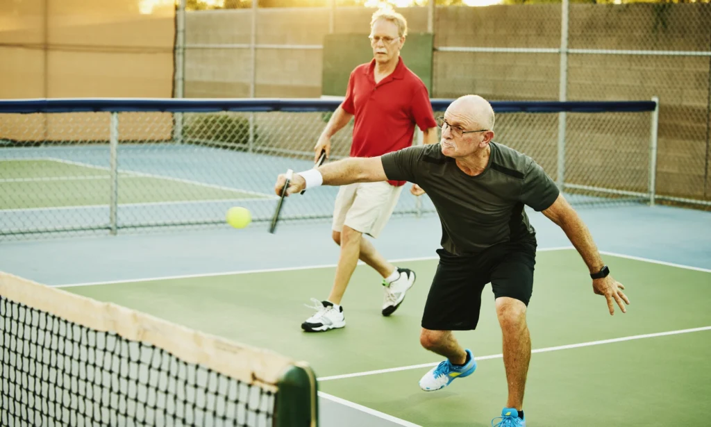 Older men playing pickleball outdoors during bright daylight.