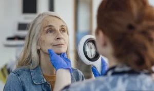 Dermatology provider examining an older patient’s facial skin to evaluate possible skin cancer treatment options.
