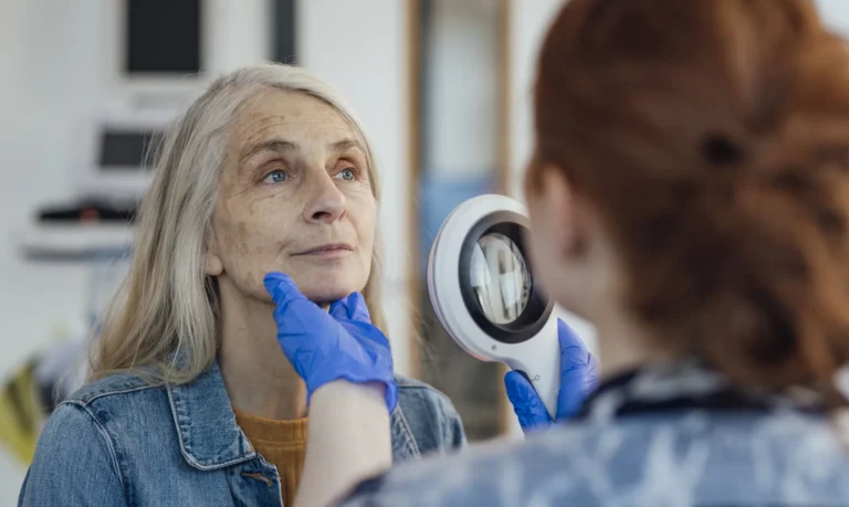 Dermatology provider examining an older patient’s facial skin to evaluate possible skin cancer treatment options.